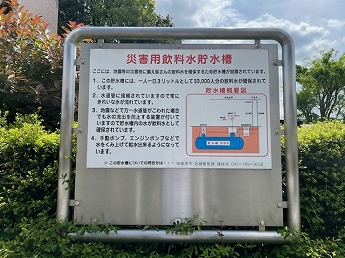 看板：災害用飲料水貯水槽　ここには、地震等の災害時に備え皆さんの飲料水を確保するため貯水槽が設置されています。